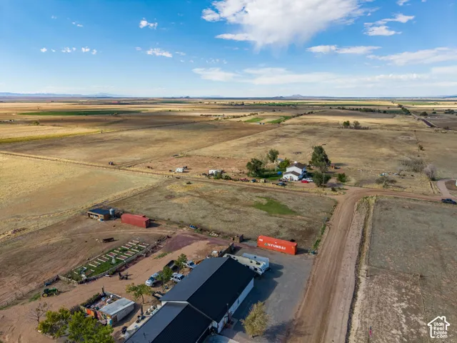 Aerial perspective of a sprawling property featuring expansive open land, a metal-roofed structure, and defined exterior acreage
