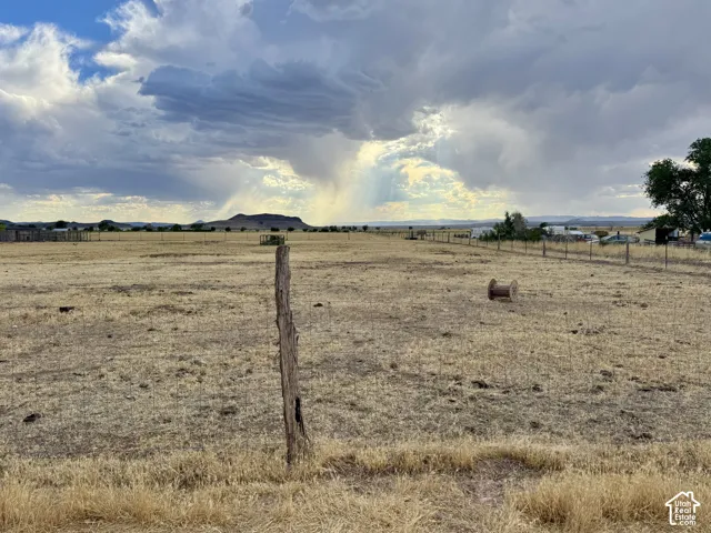 Expansive open land featuring a wire fence, distant structures, and a prominent mountain range under a cloudy sky