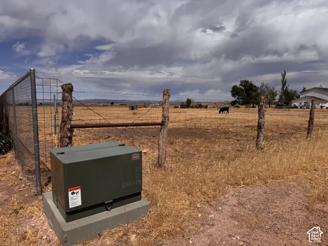 Expansive agricultural land featuring a wire fence with rustic wood posts, a metal gate, and a utility box on a concrete pad