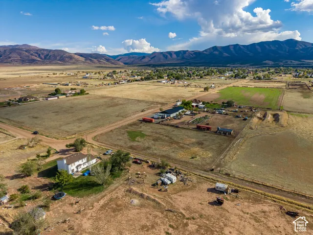 Aerial perspective of a multi-acre property featuring a detached residence, expansive open land, mountain scenery, and unpaved road access