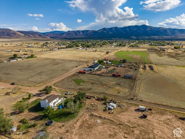 Aerial view of a multi-story residence situated on expansive acreage, featuring a prominent mountain backdrop and open terrain
