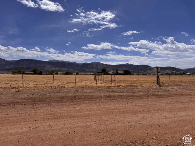 Expansive undeveloped lot featuring a natural, arid landscape and distant mountain ranges under a blue sky with scattered clouds