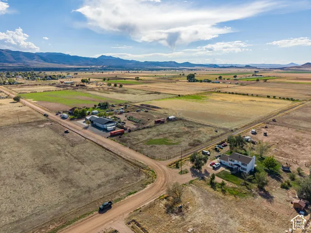 Aerial perspective of a sprawling property featuring multi-acre grounds, detached outbuildings, a prominent mountain backdrop, and expansive open terrain
