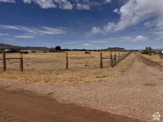 Expansive rural landscape featuring a gravel drive, a rustic wire fence, and a distant mountain range under a vast sky