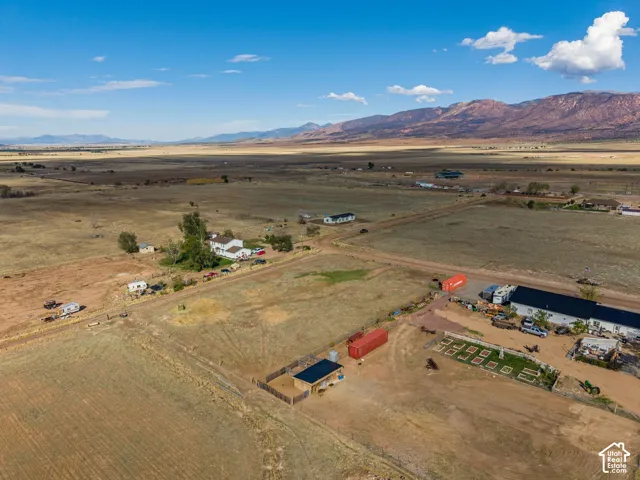 Aerial perspective of expansive acreage featuring mountain surroundings, fenced livestock areas, and established outbuildings