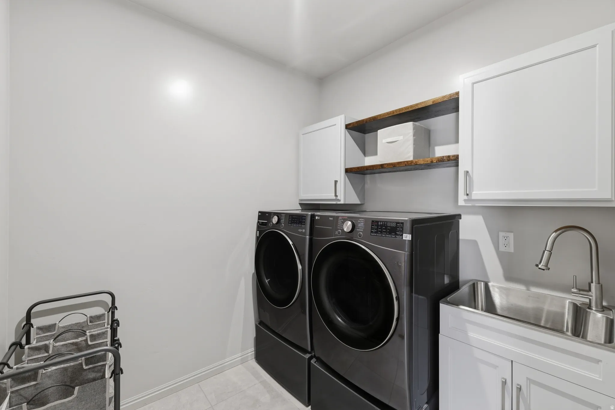 Dedicated laundry area featuring a utility sink with a brushed nickel faucet, white shaker-style cabinetry, and open wood shelving