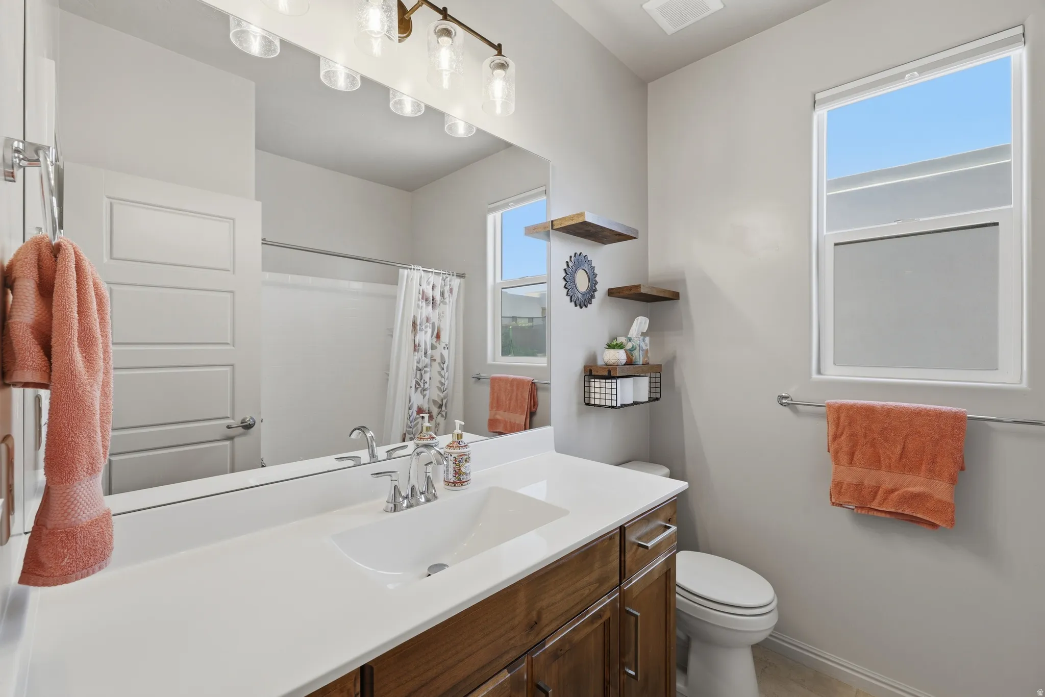 Bathroom featuring a wood-finish vanity with an integrated sink, a large wall-mounted mirror, and overhead lighting
