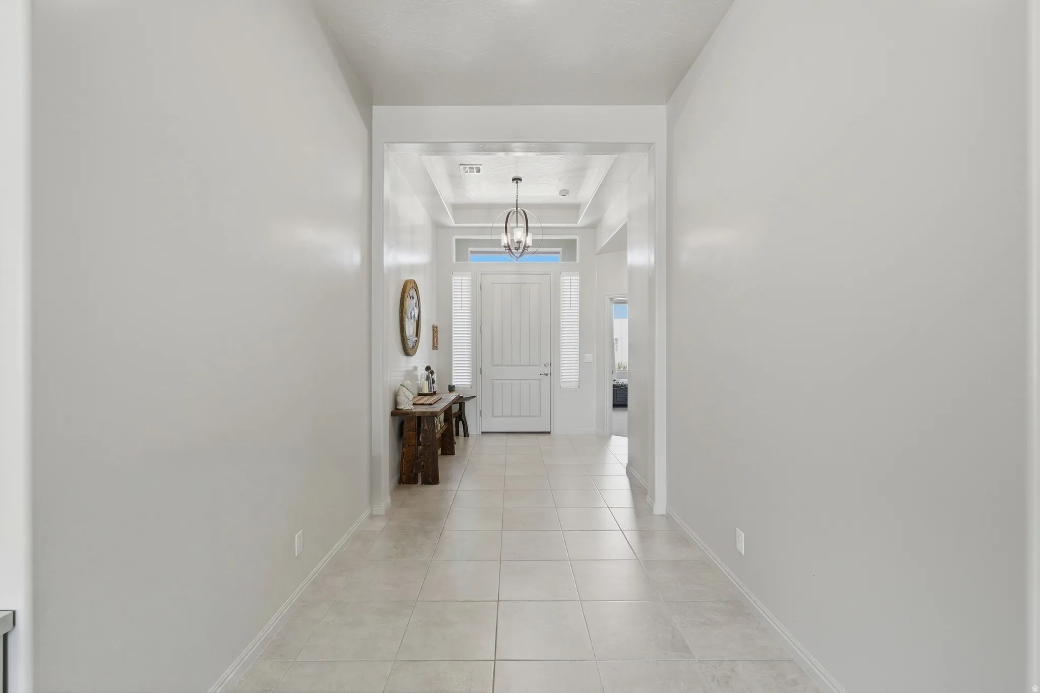 Entry foyer featuring large format tile flooring, a recessed ceiling with crown molding, and a contemporary chandelier