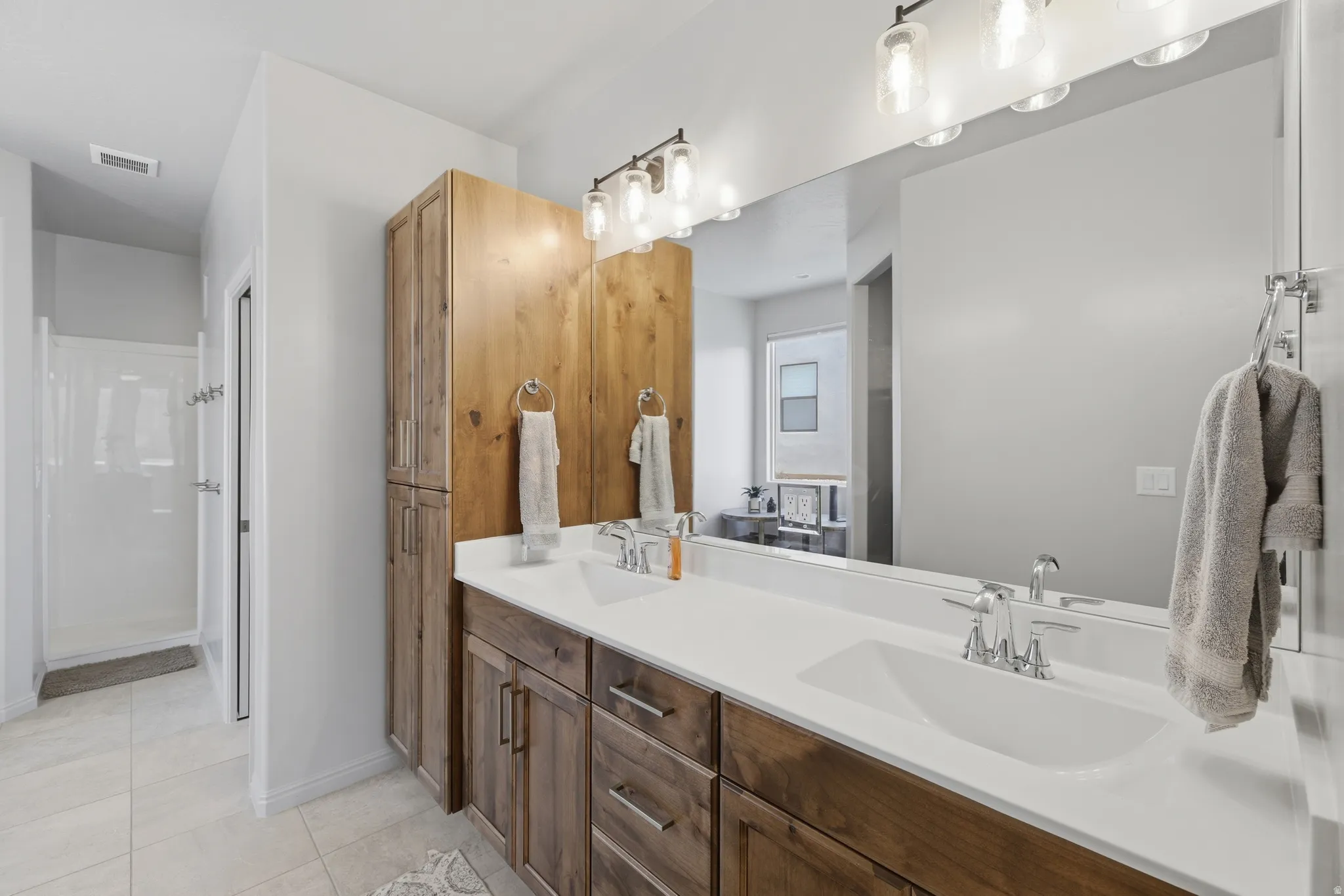 Bathroom featuring a double vanity with wood-finish cabinetry, white countertops, dual undermount sinks, and an expansive mirror