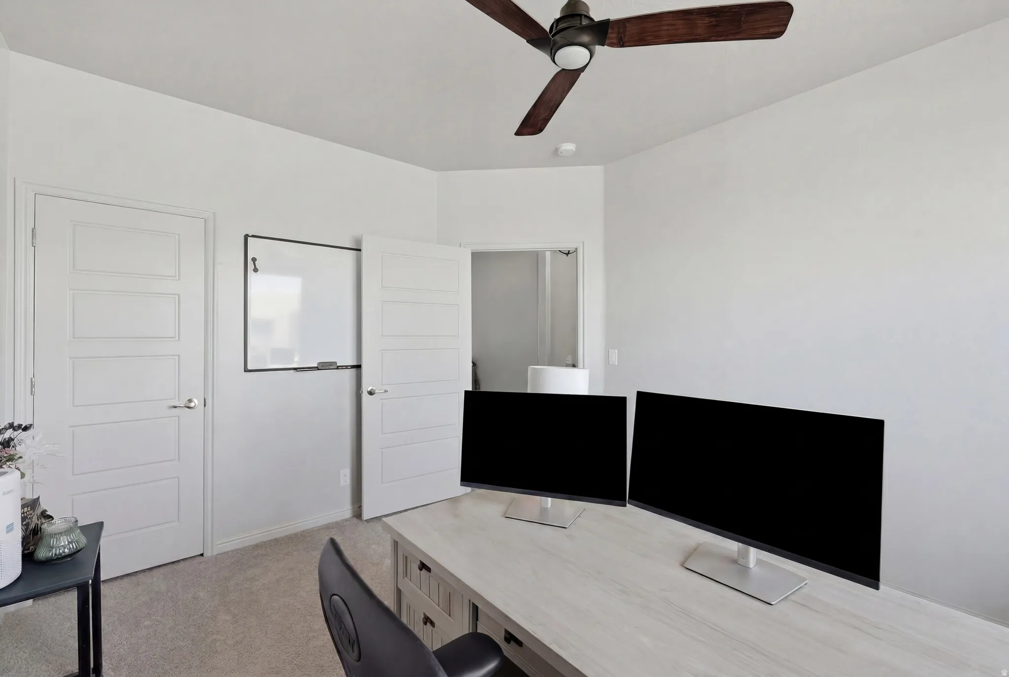 Carpeted room featuring a ceiling fan with dark wood-finish blades, white walls, and contemporary paneled doors