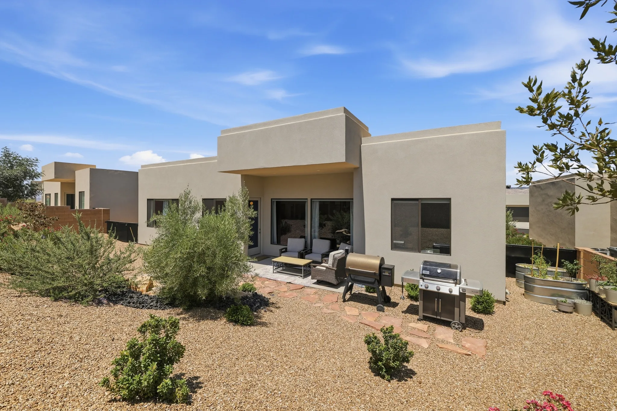 Modern desert landscaping with gravel ground cover, mature shrubs, and an outdoor patio featuring flagstone paving