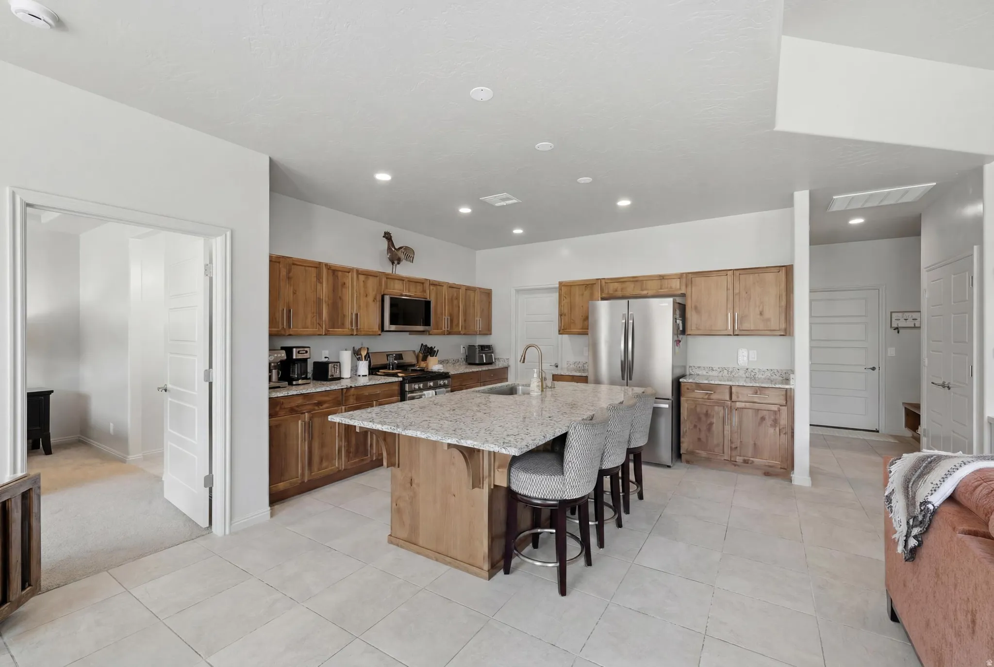 Spacious kitchen featuring light wood cabinetry, stainless steel appliances, and a central island with a stone-finish countertop