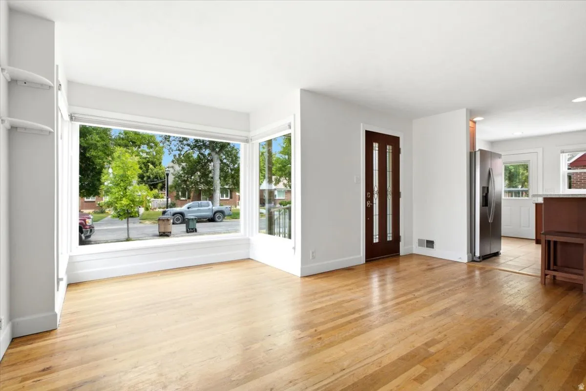 Bright living area featuring wood-finish flooring, a large picture window, and a dark wood entry door with vertical glass inserts