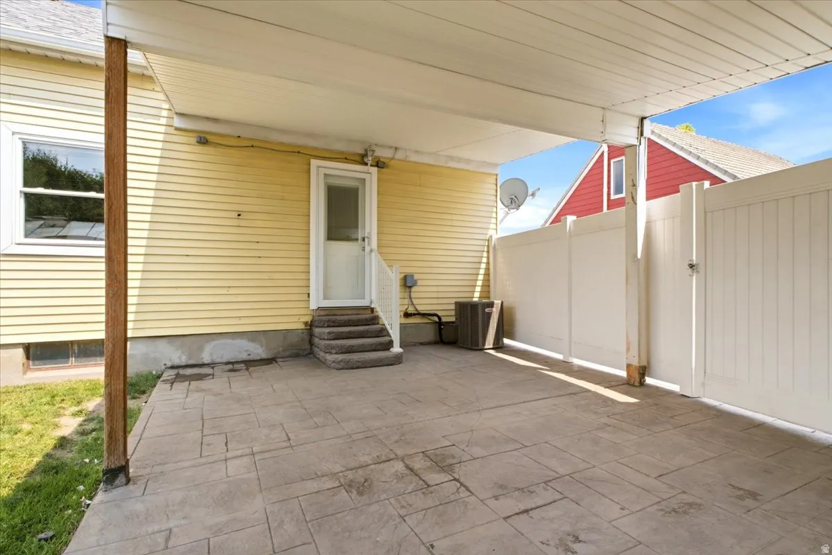 Covered outdoor patio area featuring stamped concrete flooring, a white privacy fence, and direct exterior access to the residence