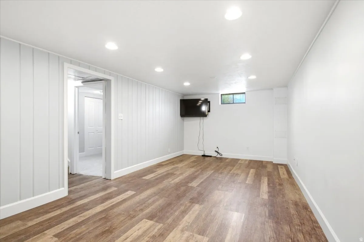 Spacious room featuring wood-finish flooring, recessed lighting, a window, and a door opening to an additional room