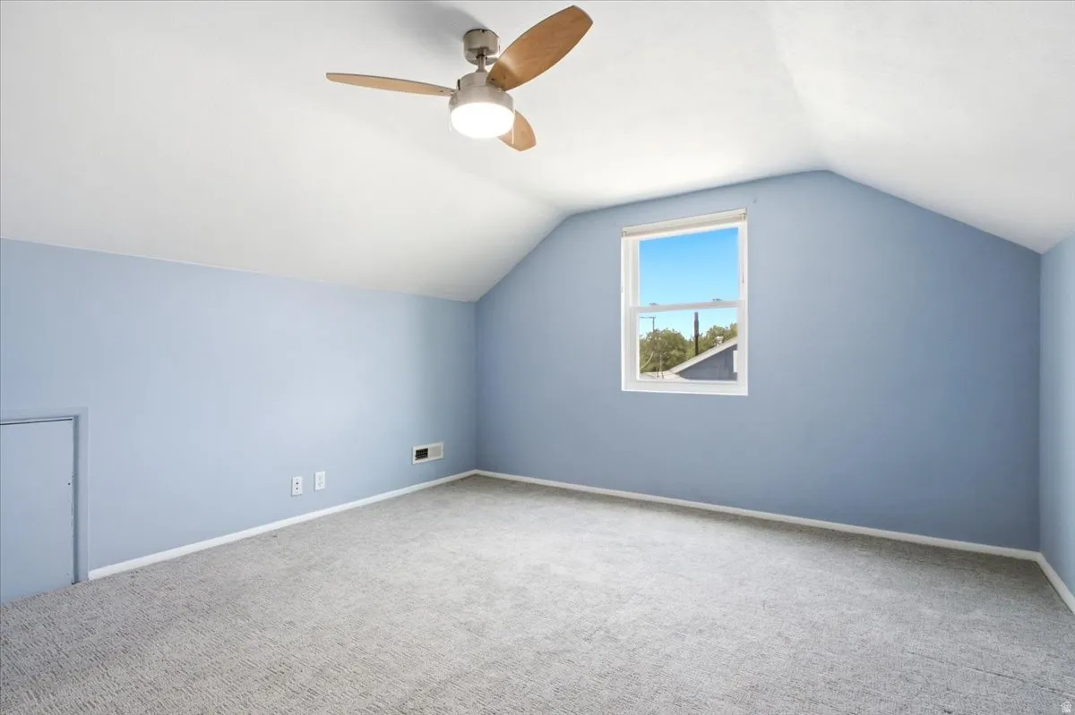 Room featuring sloped ceilings, light blue walls, and a wood-finish ceiling fan with integrated lighting