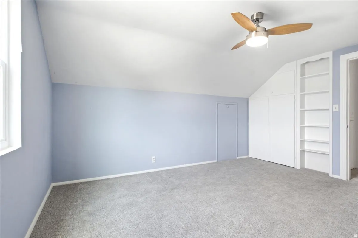 Carpeted room with a vaulted ceiling, a window, a ceiling fan with light fixture, built-in shelving, and a built-in closet with bifold doors