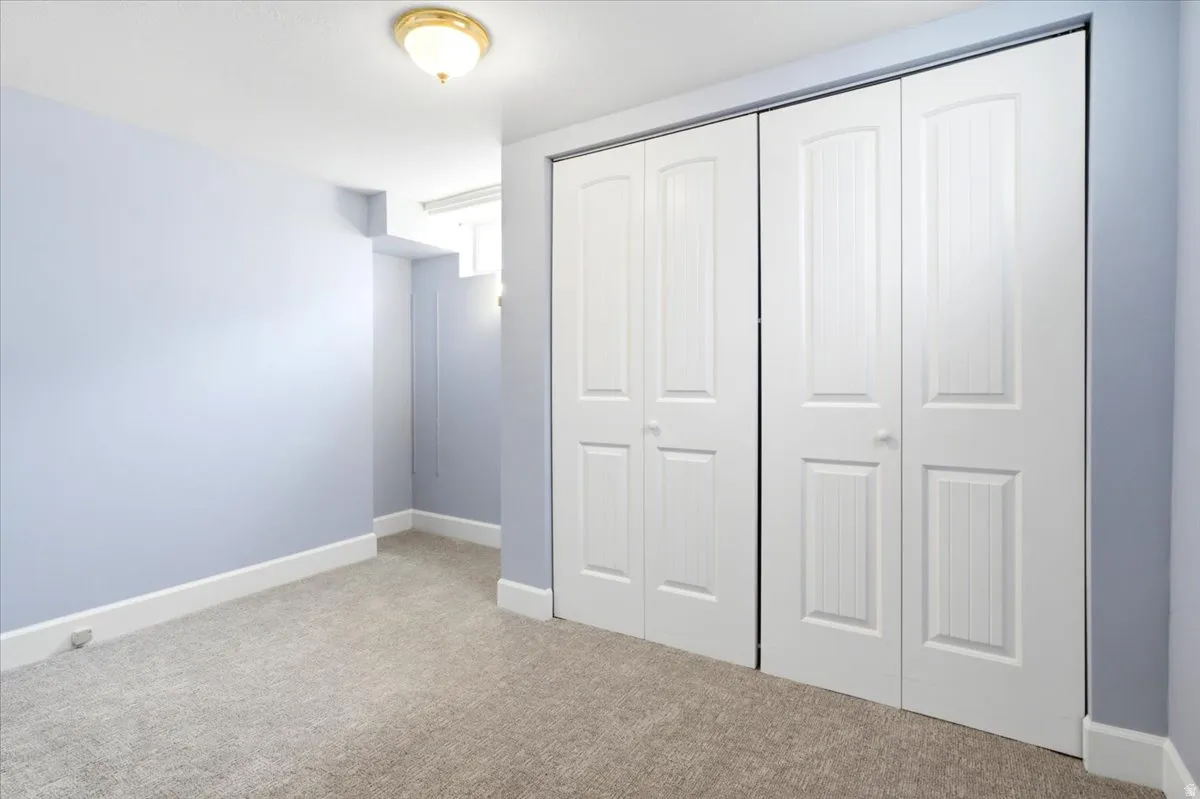 Spacious interior featuring a large closet with paneled bifold doors, light blue wall paint, white baseboards, and neutral-toned carpeting