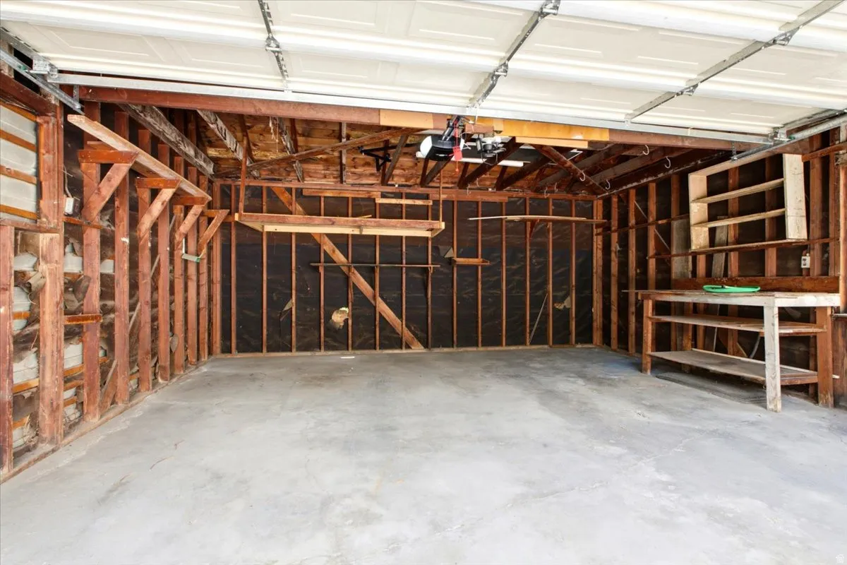 Garage interior featuring exposed wood framing, concrete flooring, overhead garage door, built-in workbench, and built-in shelving