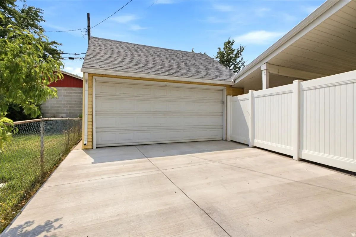 Detached garage with a paneled door, shingle roof, and yellow siding