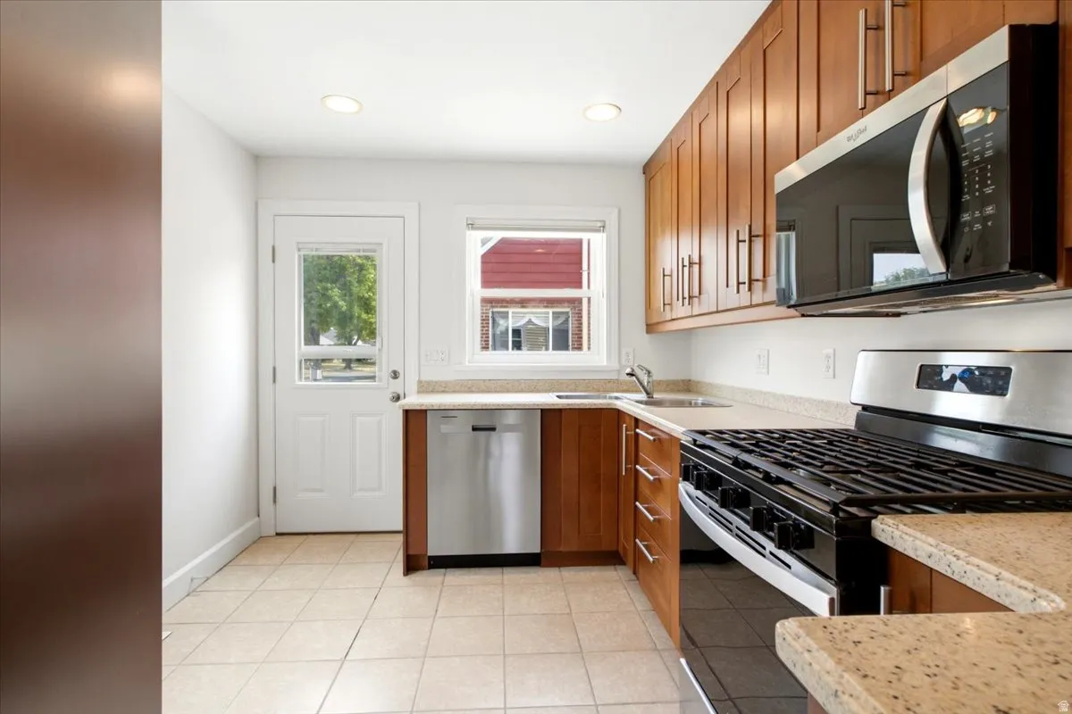 Kitchen featuring wood-finish cabinetry, stainless steel appliances, granite-style countertops, and tile flooring