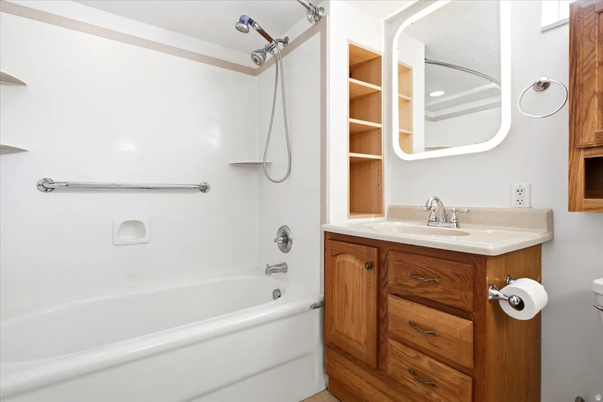 Bathroom featuring a vanity with wood-finish cabinetry, an integrated sink and countertop, and a shower-over-tub combination with a grab bar