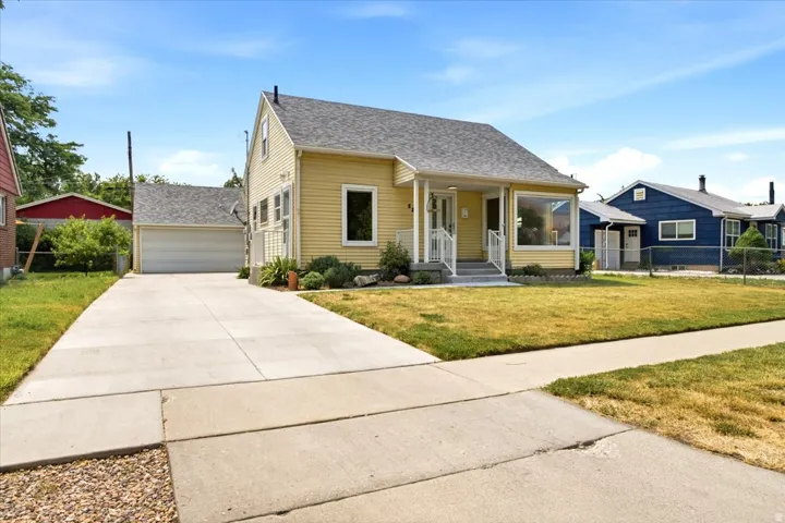 Yellow siding exterior featuring a covered porch, established landscaping, a long concrete driveway, and a detached two-car garage