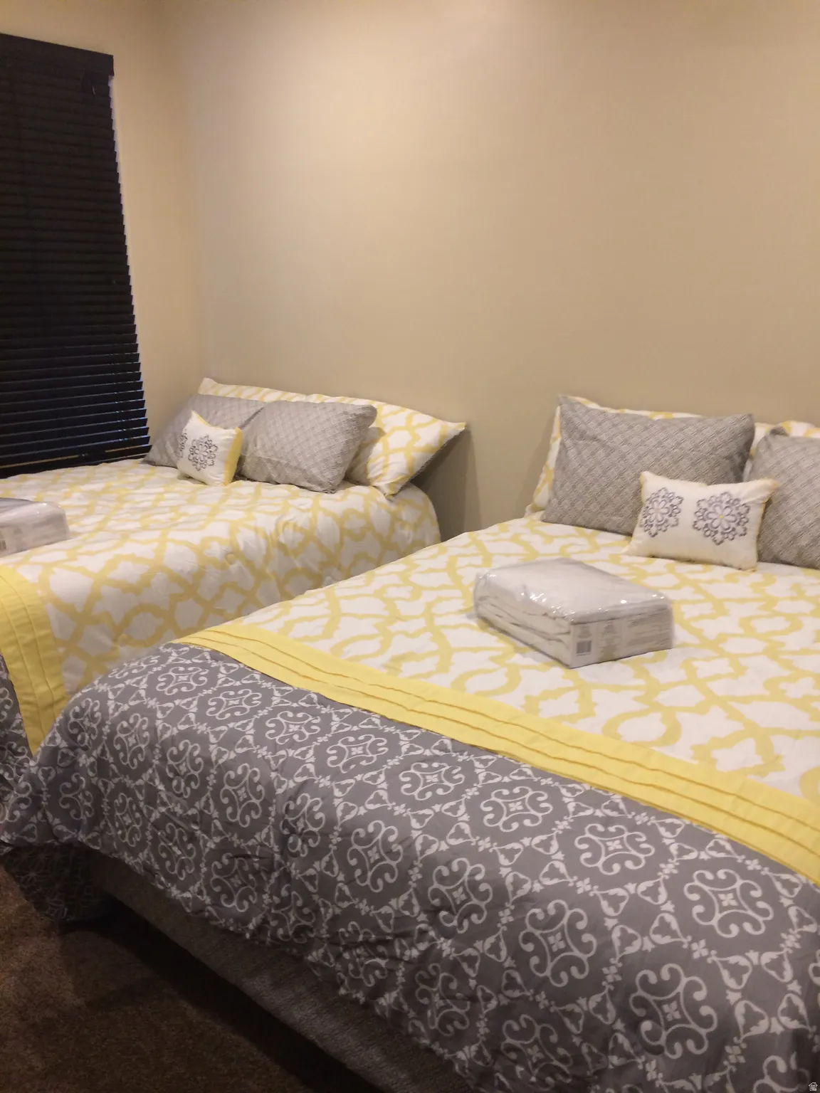 Spacious room featuring two beds with patterned bedding, neutral wall tones, and dark window blinds