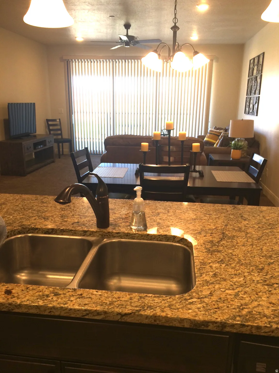 Kitchen counter featuring a dual basin stainless steel sink with a dark bronze faucet, granite-finish countertop, and dark wood-finish cabinetry