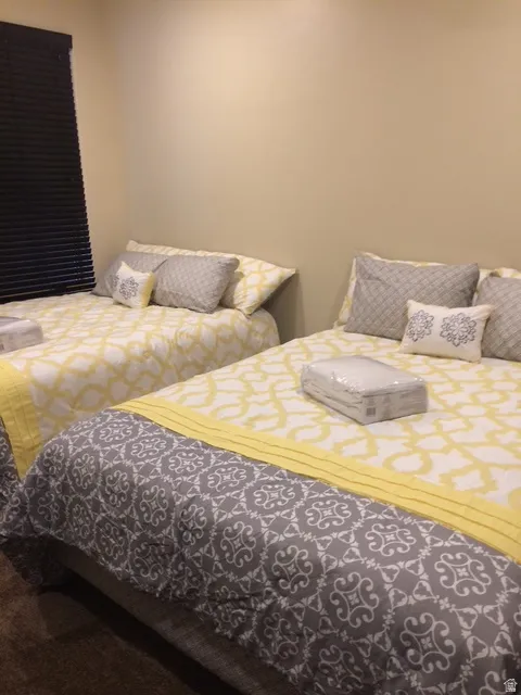 Two beds with patterned bedding and throw pillows within a room featuring warm-toned walls and dark window blinds