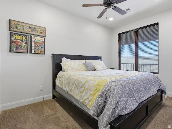 Spacious room featuring a dark-finish ceiling fan with integrated lighting, a large window with horizontal blinds, neutral carpet flooring, and white baseboards