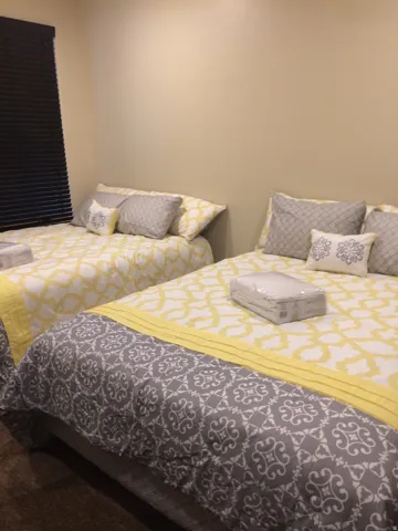 Spacious room featuring two beds with patterned bedding, neutral wall tones, and dark window blinds
