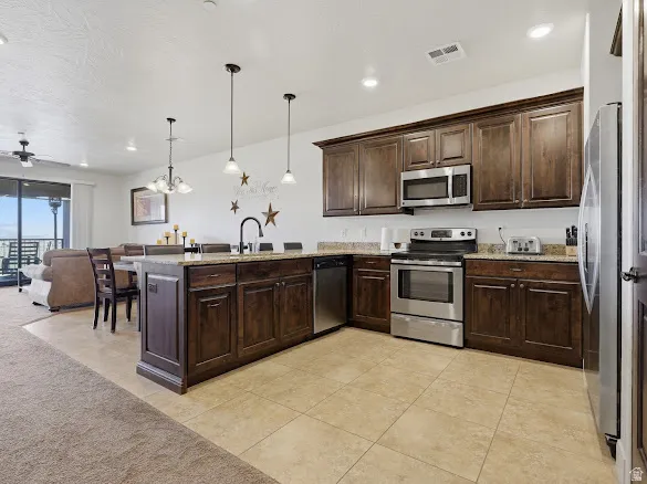 Open concept kitchen featuring dark wood cabinetry, stainless steel appliances, granite countertops, and tile flooring