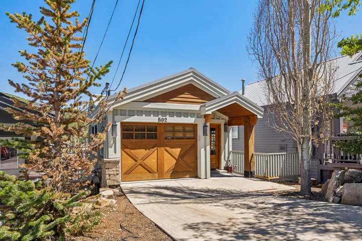 Exterior featuring a wood-finish garage door, stone accents, horizontal siding, and a covered entry with a railing