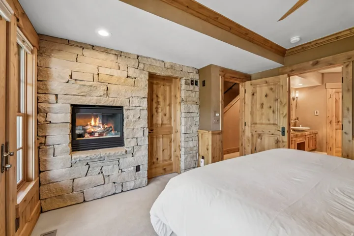 Bedroom featuring a stone-clad fireplace and light wood doors