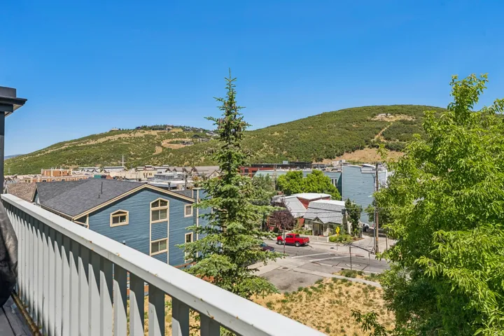 Balcony with white vertical railing overlooking a neighborhood with varied architecture and distant green hills
