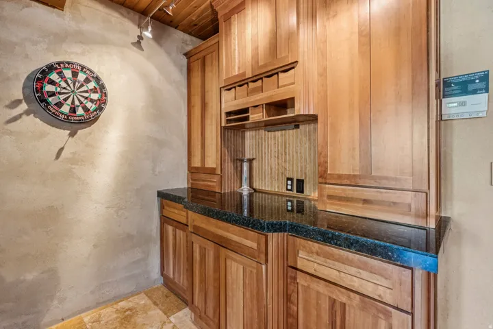 Built-in wood cabinetry with a dark stone-finish countertop, under-cabinet lighting, and a textured backsplash