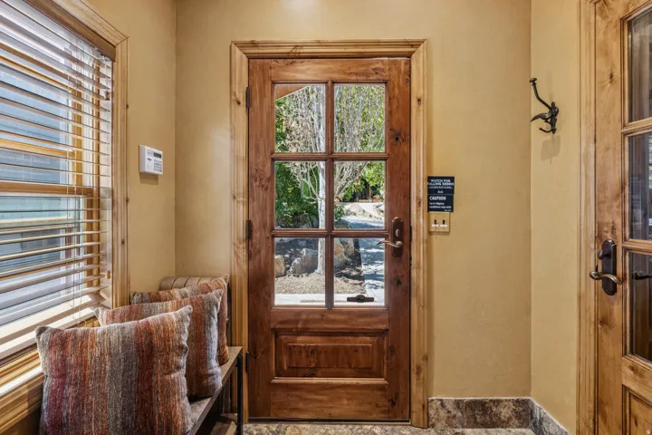 Entryway featuring a wood-panel door with glass lites, wood-finish window blinds, and stone tile flooring