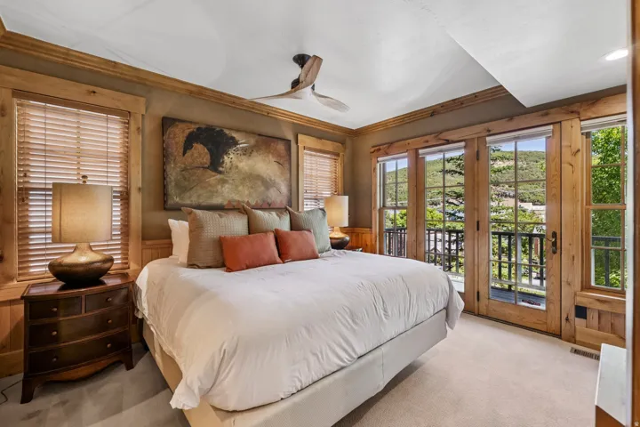 Spacious bedroom featuring light-toned carpeting and wood-clad french doors opening to a balcony