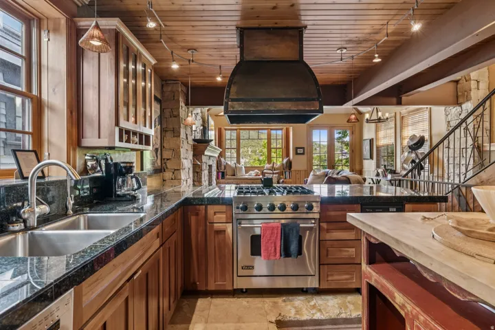 Gourmet kitchen featuring a stainless steel gas range, stone countertops, natural wood cabinetry, and a custom range hood