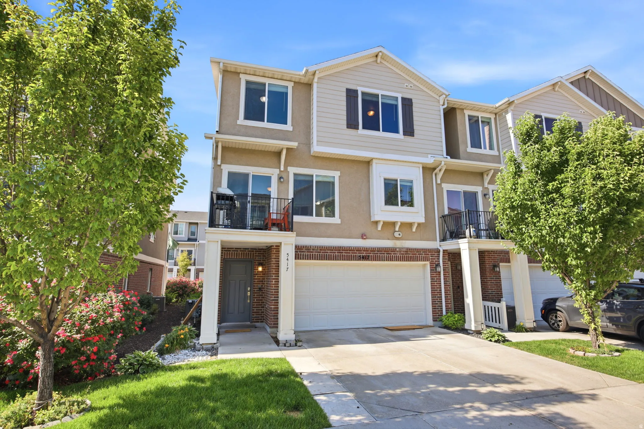 Three-story townhome featuring a two-car garage, brick facade detailing, and a second-story balcony