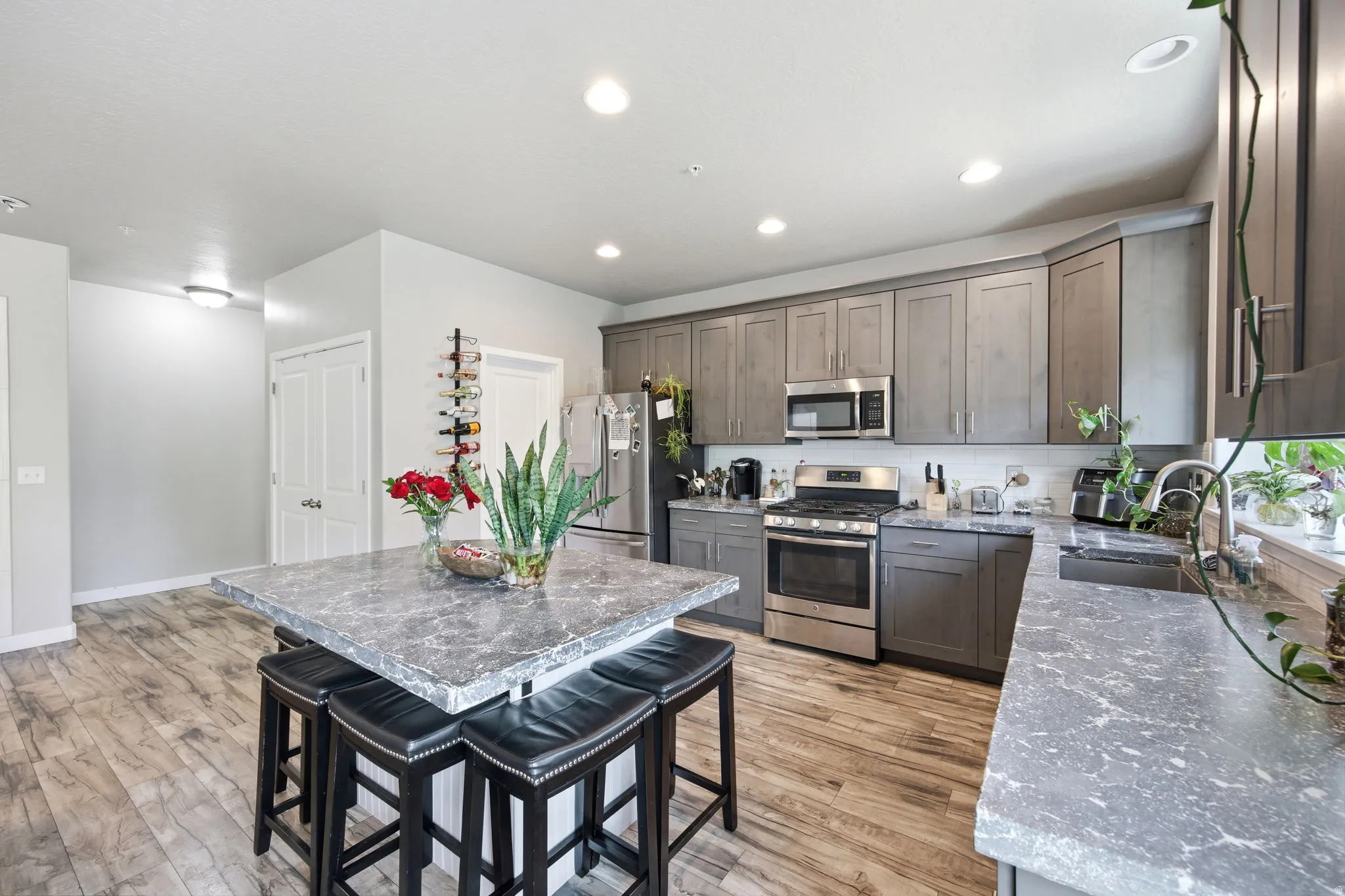 Spacious kitchen featuring a large island with seating, grey cabinetry, stainless steel appliances, and wood-finish flooring