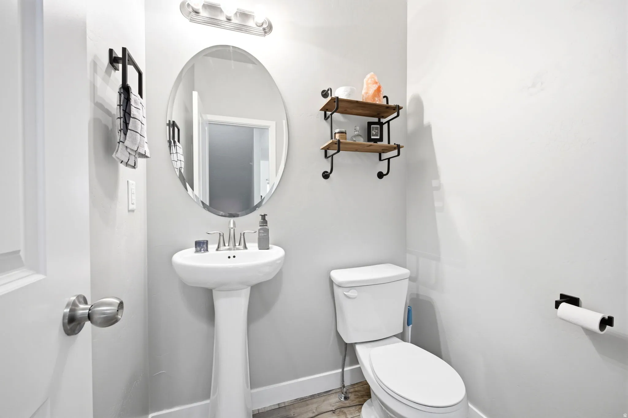 Modern powder room featuring a white pedestal sink, an oval mirror, and a three-light vanity fixture