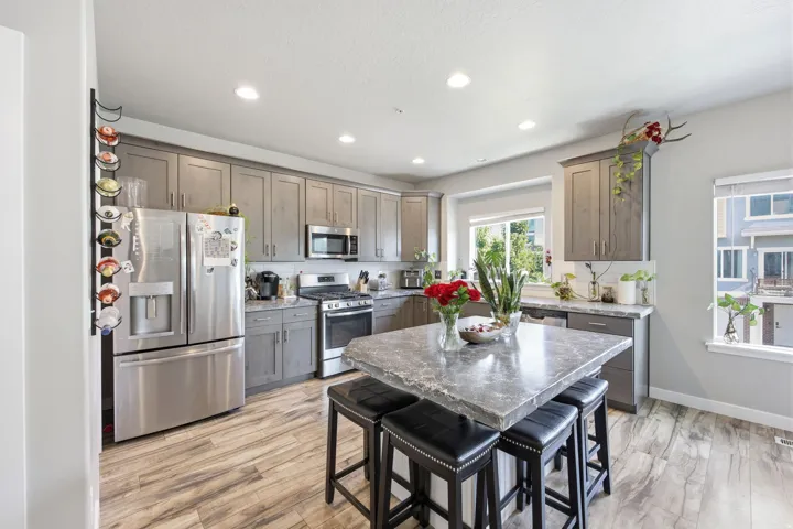 Kitchen featuring grey cabinetry, stainless steel appliances, a center island with a stone countertop, and wood-finish flooring