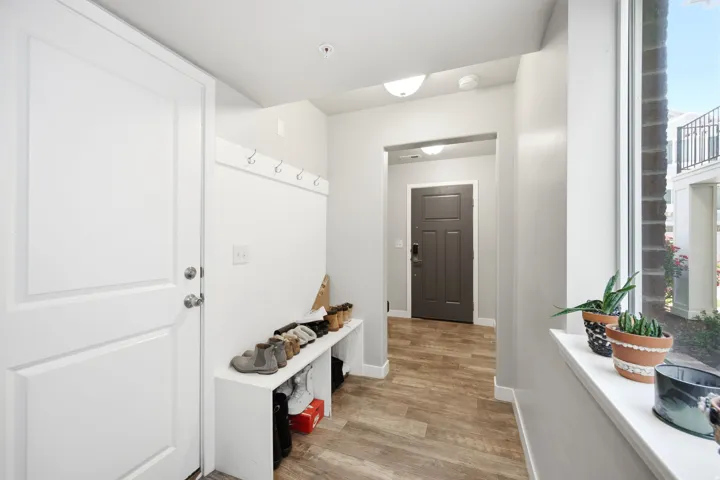 Entryway with wood-finish flooring, a white paneled door, built-in coat hooks, and a large window