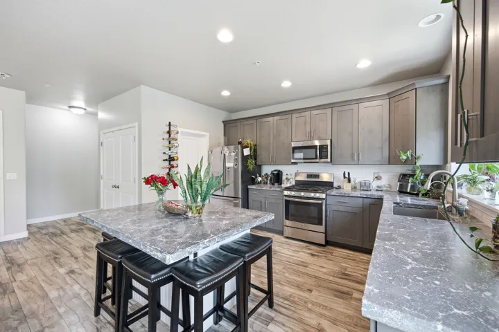 Spacious kitchen featuring a large island with seating, grey cabinetry, stainless steel appliances, and wood-finish flooring