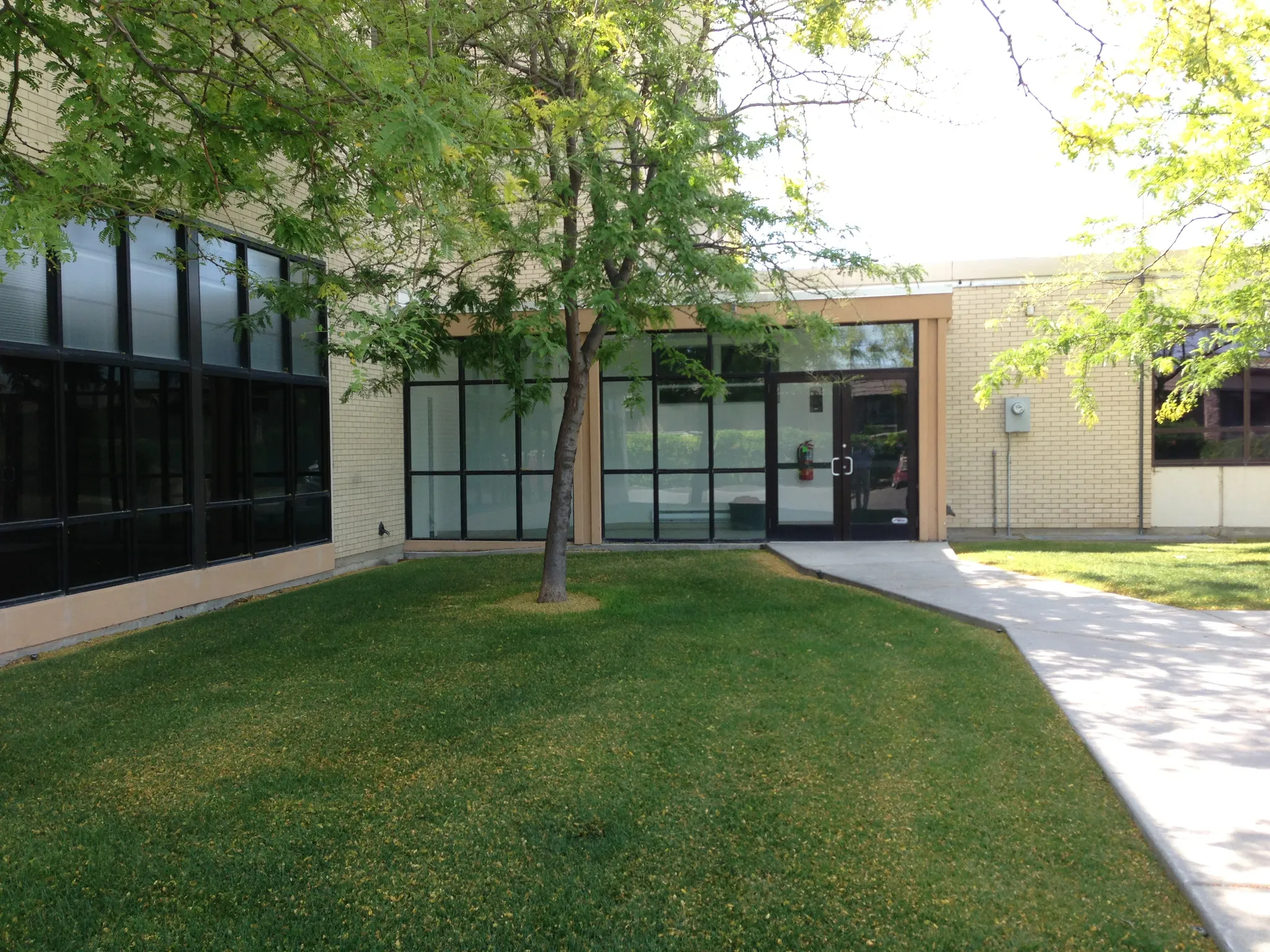 Brick exterior building with multiple large window panes, a central glass entrance, and a concrete pathway
