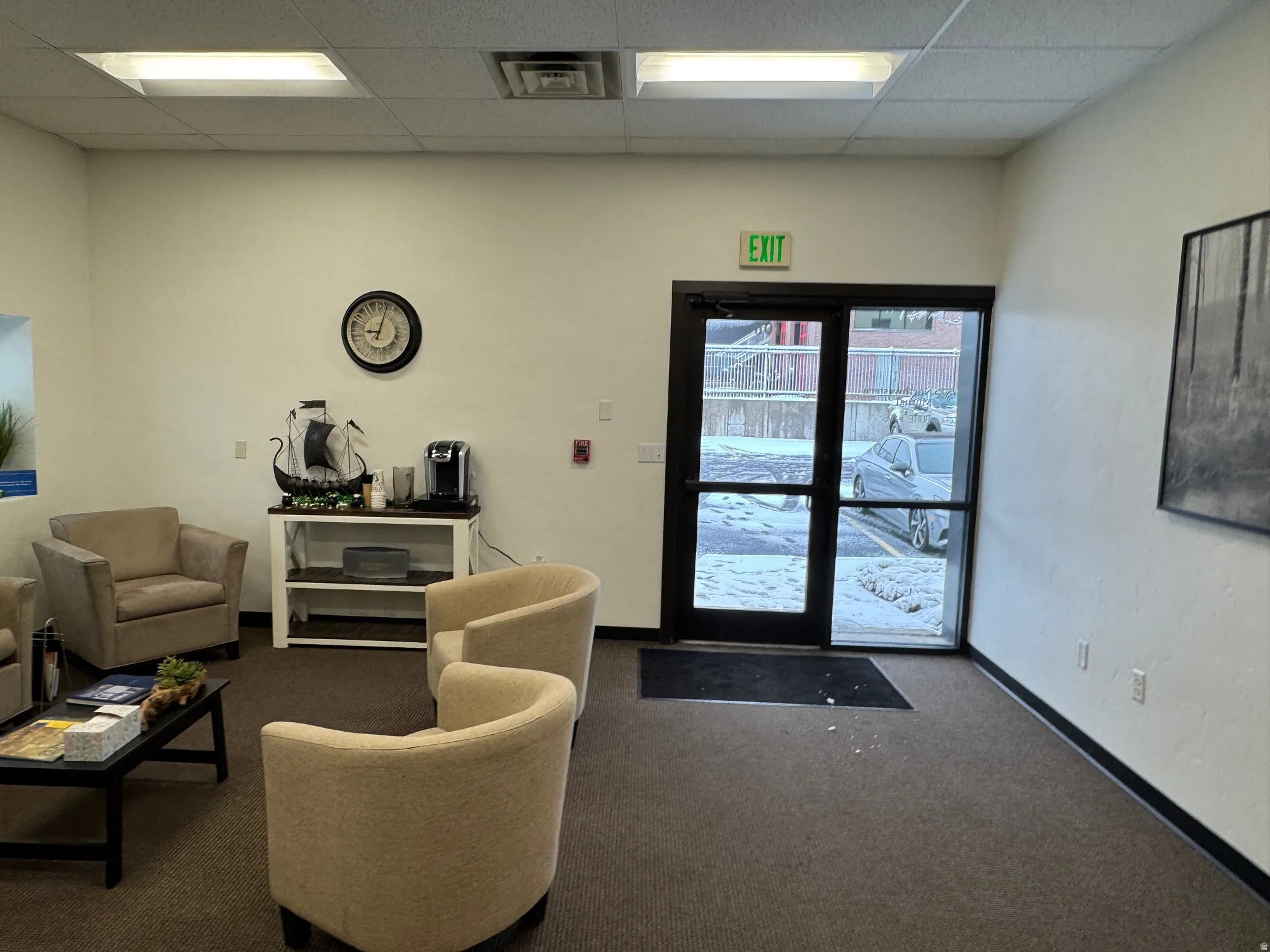 Commercial interior featuring a glass-paneled entry door, dropped ceiling with integrated lighting, and neutral-toned carpeting