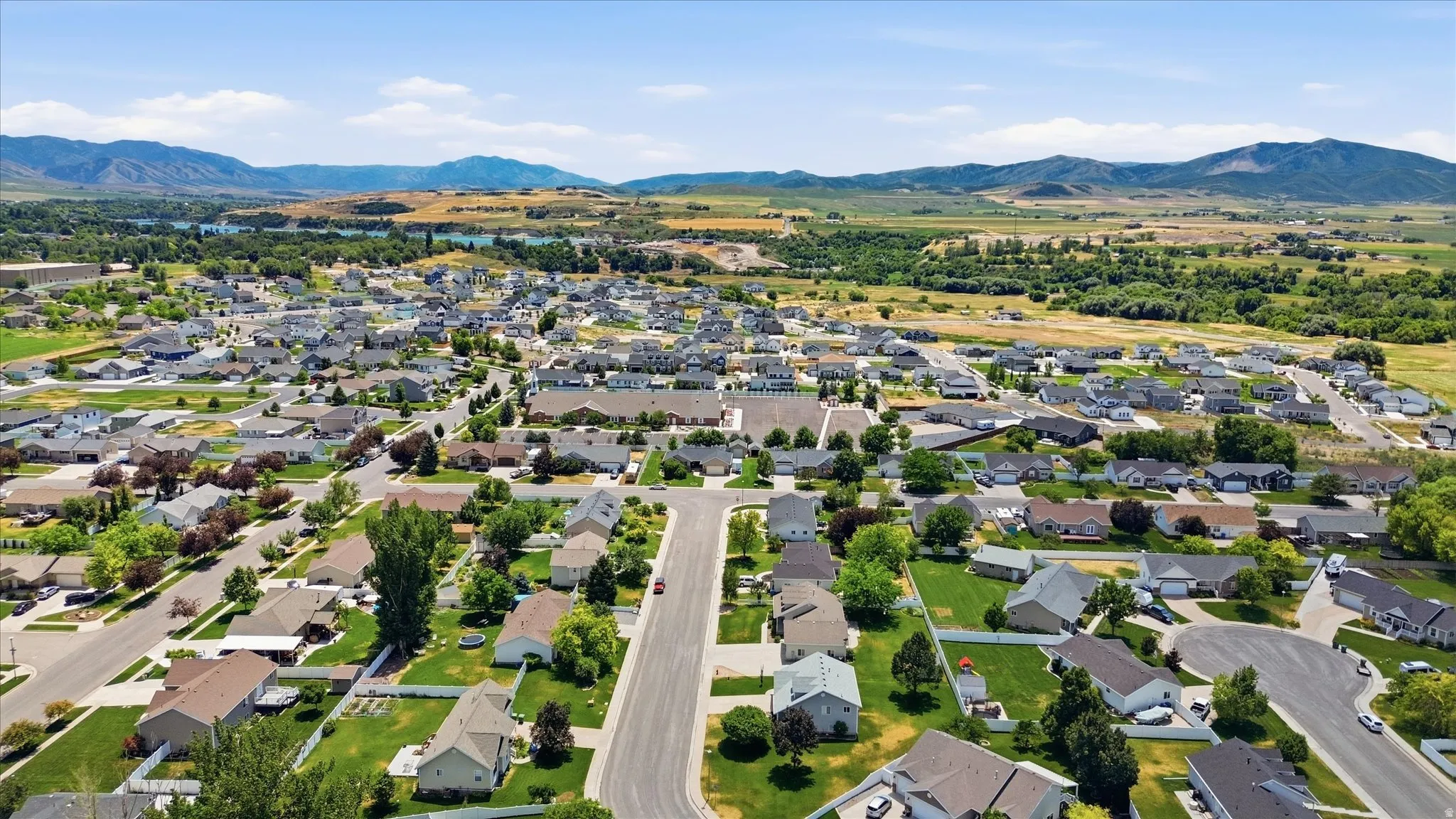 Expansive aerial panorama showcasing a residential neighborhood with a backdrop of distant mountains and a body of water