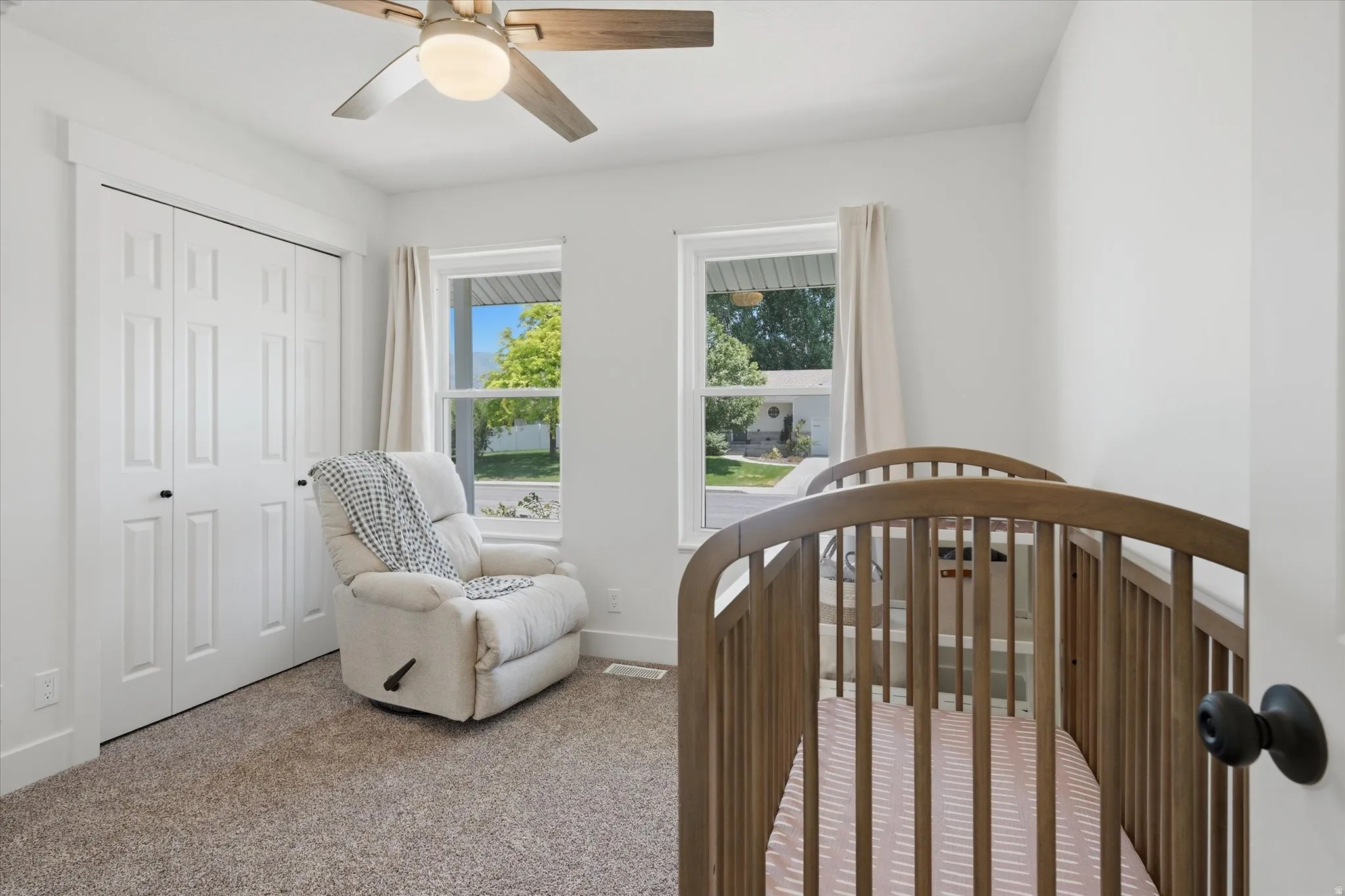 Bright room featuring two windows, neutral carpeting, a ceiling fan with integrated lighting, and bi-fold closet doors